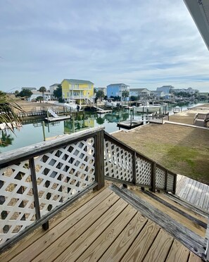 A wooden deck with a lattice railing overlooking a marina with boats and colorful buildings in the background. - Canal-front 3 Bed 2 Bath home including a dock. (Holden Beach)