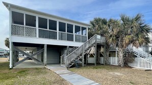 A two-story house with a covered porch and a wooden staircase leading to a deck. - Canal-front 3 Bed 2 Bath home including a dock. (Holden Beach)