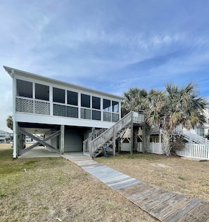 A two-story house with a covered porch and a wooden staircase leading to a deck. - Canal-front 3 Bed 2 Bath home including a dock. (Holden Beach)