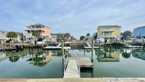 A marina with docked boats, a wooden pier, and multi-story buildings with balconies. - Canal-front 3 Bed 2 Bath home including a dock. (Holden Beach)