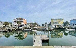 A marina with docked boats, a wooden pier, and multi-story buildings with balconies. - Canal-front 3 Bed 2 Bath home including a dock. (Holden Beach)