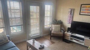 Ein Wohnzimmer mit einer Couch, Couchtisch, TV-Schrank und Fenstern mit Jalousien.