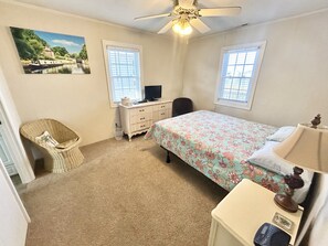Ein Schlafzimmer mit Bett, Kommode, Stuhl, Schreibtisch und Deckenventilator.