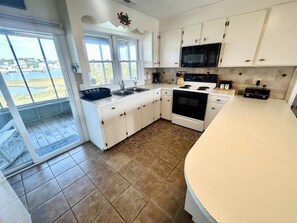 A kitchen with white cabinets, a black microwave, and a stove. - Canal-front 4BR, 2BA Holden Beach retreat with dock (Holden Beach)