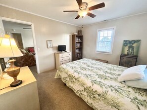 A bedroom with a bed, a ceiling fan, a bookshelf, a desk with a lamp, and a window. - Canal-front 4BR, 2BA Holden Beach retreat with dock (Holden Beach)