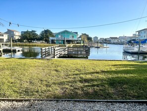 A waterfront property with a dock, grassy areas, and a building with a blue facade. - Canal-front 4BR, 2BA Holden Beach retreat with dock (Holden Beach)