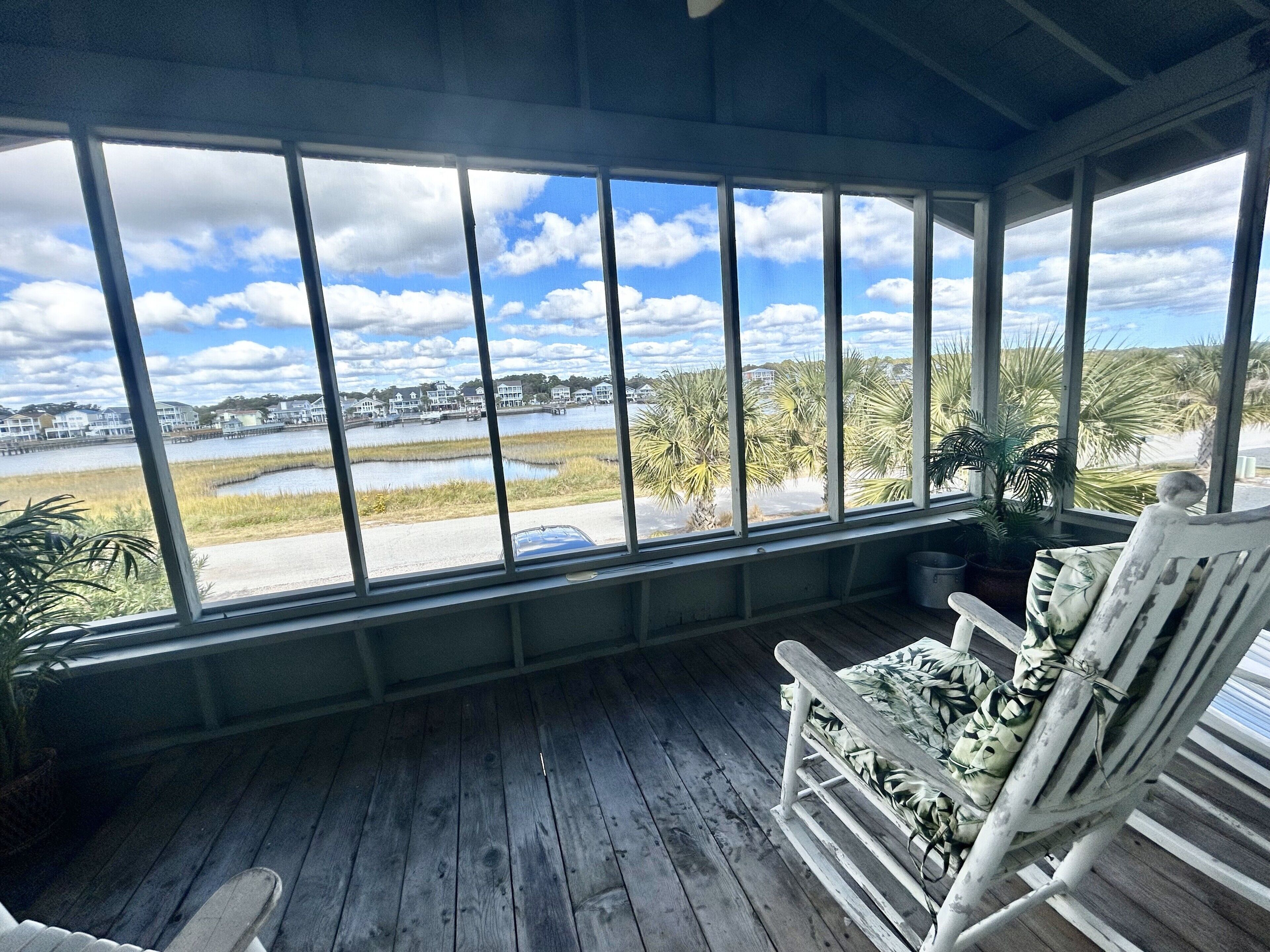 Un porche techado con vista a un lago, casas y palmeras.