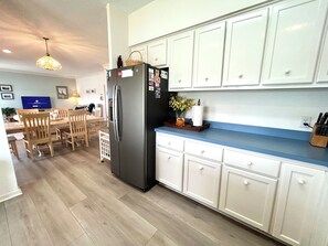 A modern kitchen with white cabinets, a stainless steel refrigerator, wooden dining table, and chairs. - Waterfront 4 bedroom retreat with dock and porch swing! (Holden Beach)