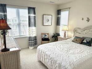 A bedroom with a bed, two bedside tables, a chair, a lamp, a framed picture, and curtains. - Waterfront 4 bedroom retreat with dock and porch swing! (Holden Beach)