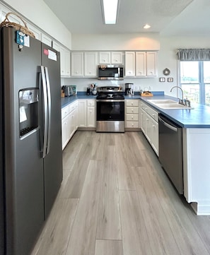 A modern kitchen with a refrigerator, stove, microwave, and sink. - Waterfront 4 bedroom retreat with dock and porch swing! (Holden Beach)