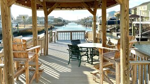 A wooden deck with outdoor seating, a view of a body of water, and a building in the background. - Spacious 3-bedroom, 2-bath canal home located with Canal access and Waterway views. (Supply)