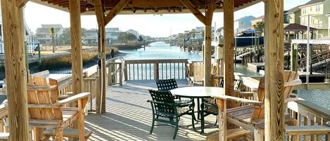 A wooden deck with outdoor seating, a view of a body of water, and a building in the background.