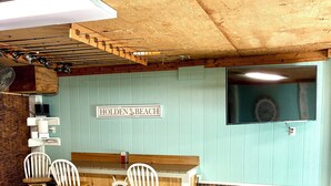 A bar area with a sign reading 'HOLDEN BEACH,' two white bar stools, a wooden counter, and a brick wall. - Spacious 3-bedroom, 2-bath canal home located with Canal access and Waterway views. (Supply)