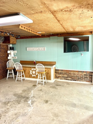 A bar area with a sign reading 'HOLDEN BEACH,' two white bar stools, a wooden counter, and a brick wall. - Spacious 3-bedroom, 2-bath canal home located with Canal access and Waterway views. (Supply)