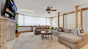 Ein Wohnzimmer mit Ecksofa, rundem Couchtisch, Kamin und an der Wand befestigtem Fernseher.
