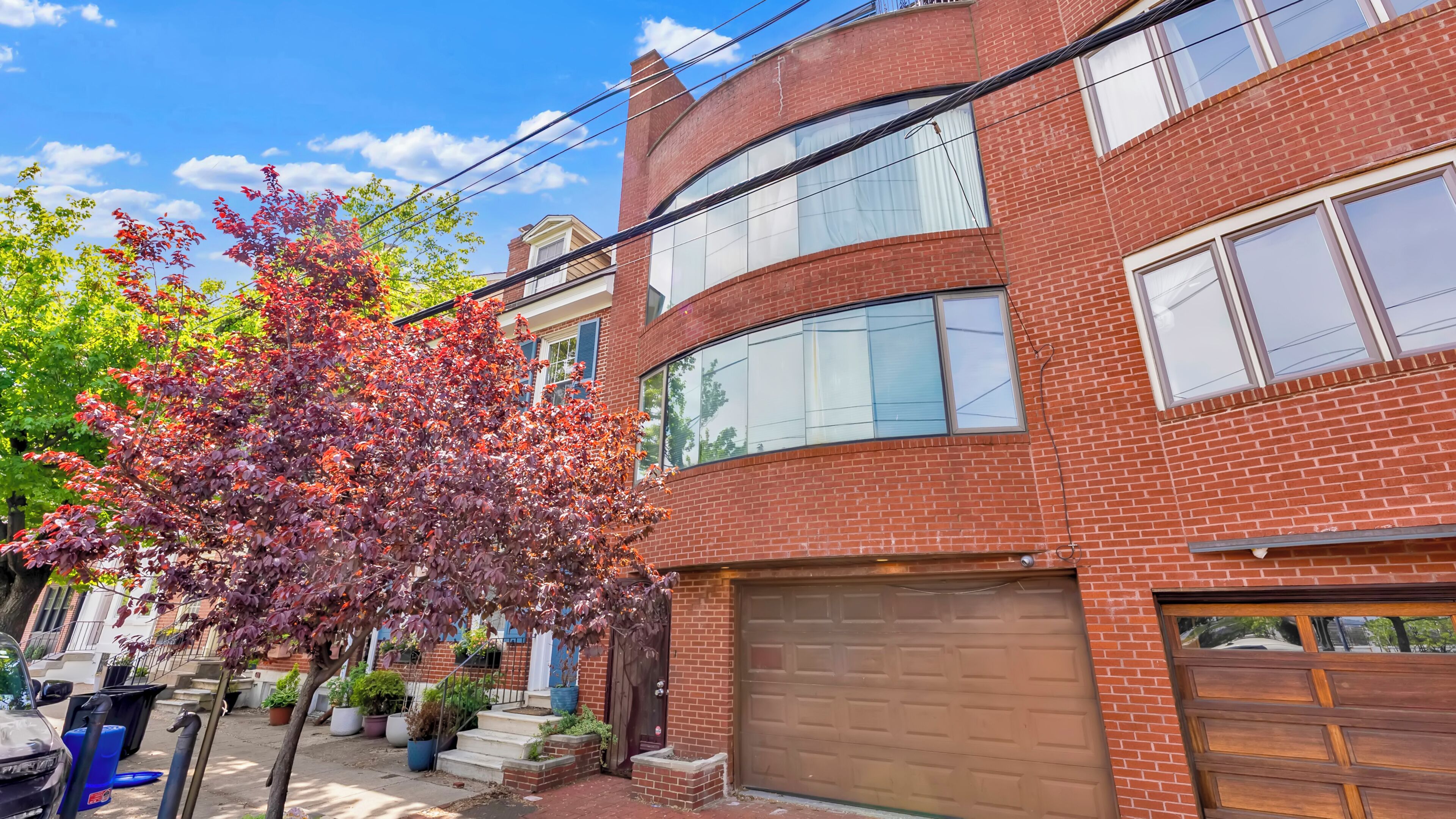 A two-story brick building with a garage, a tree with red leaves, and a clear blue sky.