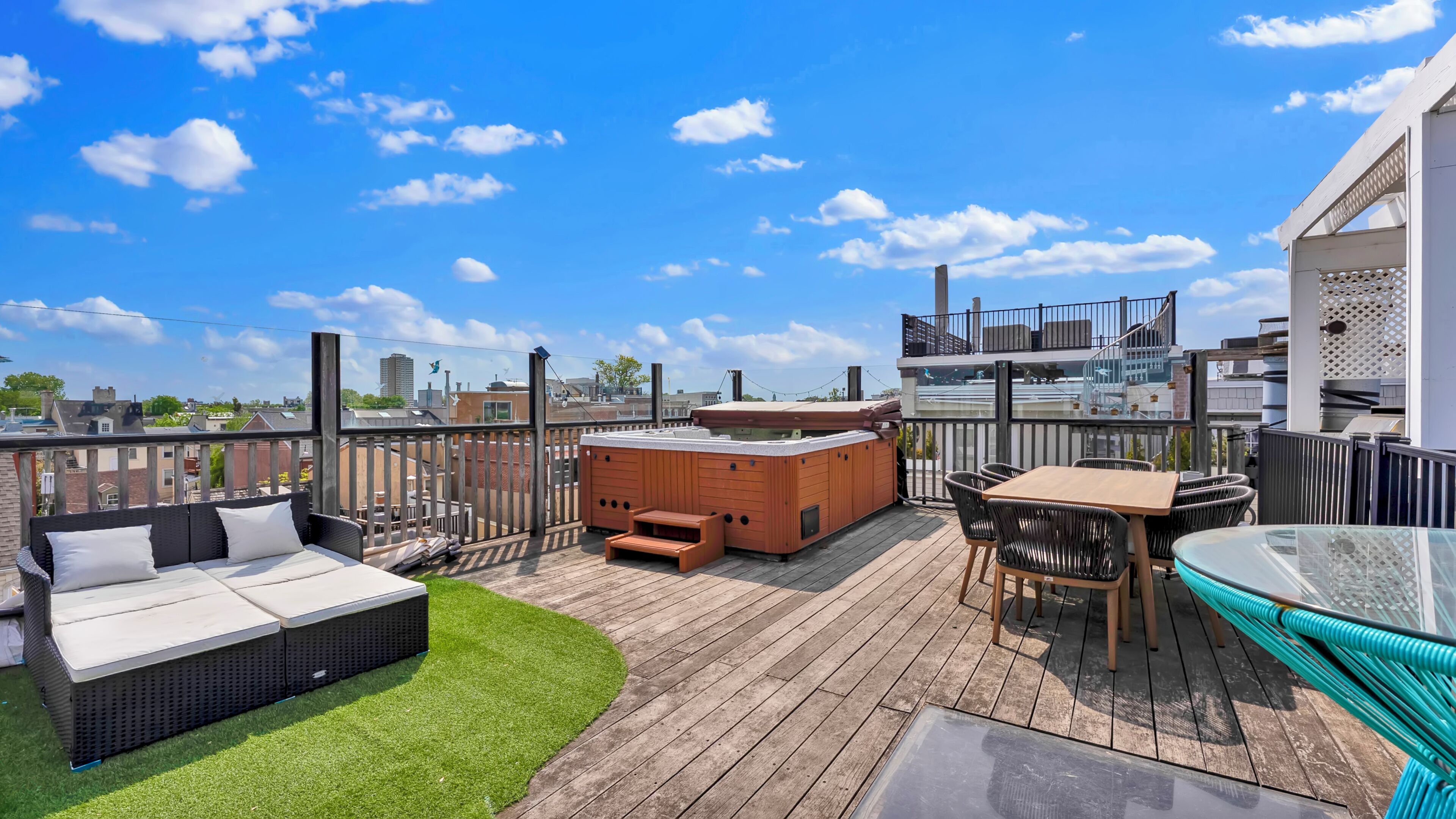 A rooftop deck with a hot tub, outdoor seating, and a glass table.