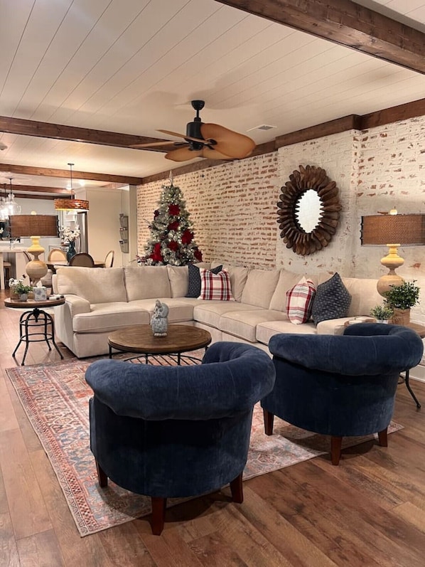 Ein Wohnzimmer mit einem Ecksofa, zwei Sesseln, einem Couchtisch, einem Kamin, einem Weihnachtsbaum und einer Ziegelwand.