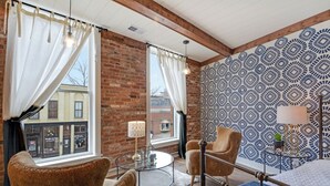 Een kamer met een bakstenen muur, behang met een patroon, een ronde tafel met stoelen en uitzicht op de straat.