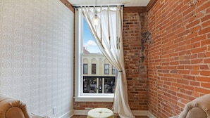 Een hoekzaal met een bakstenen muur, een raam met witte gordijnen en twee gestoffeerde fauteuils.