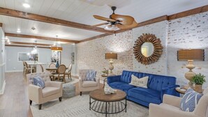 A living room with a blue sofa, beige armchairs, a coffee table, and a dining area with a chandelier. - Elle & Becks Second Floor Suite (Galena)