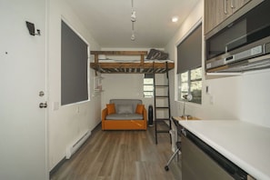 A compact kitchen with a built-in oven, a ladder, and a small sofa.