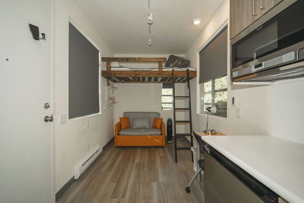 A compact kitchen with a built-in oven, a ladder, and a small sofa.