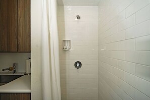 A bathroom with white tiled walls, a shower with a control panel, and a wooden cabinet.