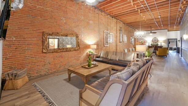 A spacious living area with a brick wall, a ceiling fan, and a wooden floor.
