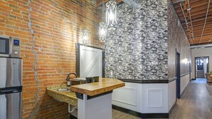 A kitchen with a brick wall, a stainless steel refrigerator, a wooden countertop, and a backsplash with a leaf pattern.
