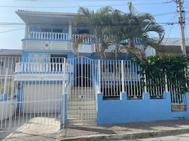 Um edifício de dois andares com fachada azul, entrada protegida por grades e uma varanda.