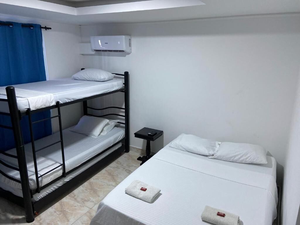A dormitory room with bunk beds, a small table, a nightstand, and an air conditioning unit.