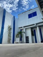 Um edifício com fachada branca e detalhes em azul, uma cadeira branca do lado de fora e uma palmeira.