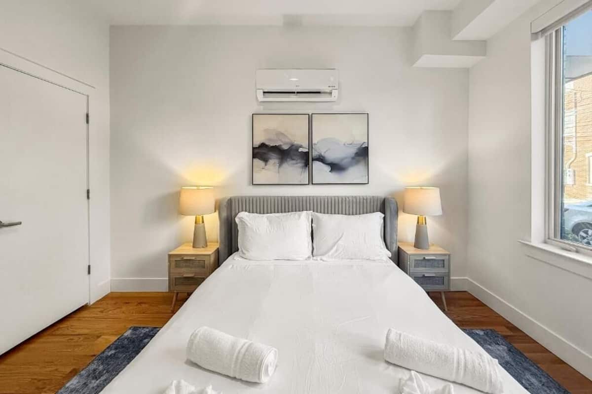Une chambre d’hôtel avec un grand lit, deux lampes de chevet, un climatiseur et deux tableaux abstraits accrochés au mur.