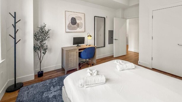 Habitació d'hotel amb un llit, un escriptori amb un ordinador, una cadira, una petita planta i un mirall a la paret.