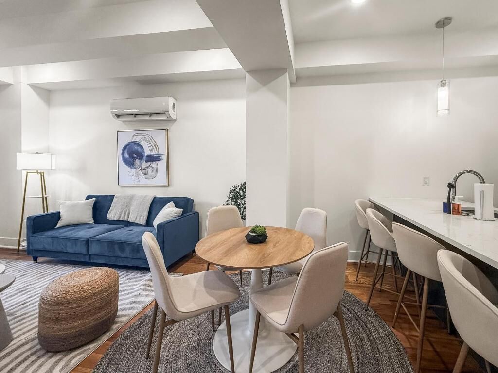 A modern living room with a blue sofa, a round wooden table, and white chairs.