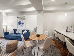 Ein modernes Wohnzimmer mit einem blauen Sofa, einem runden Holztisch und weißen Stühlen.