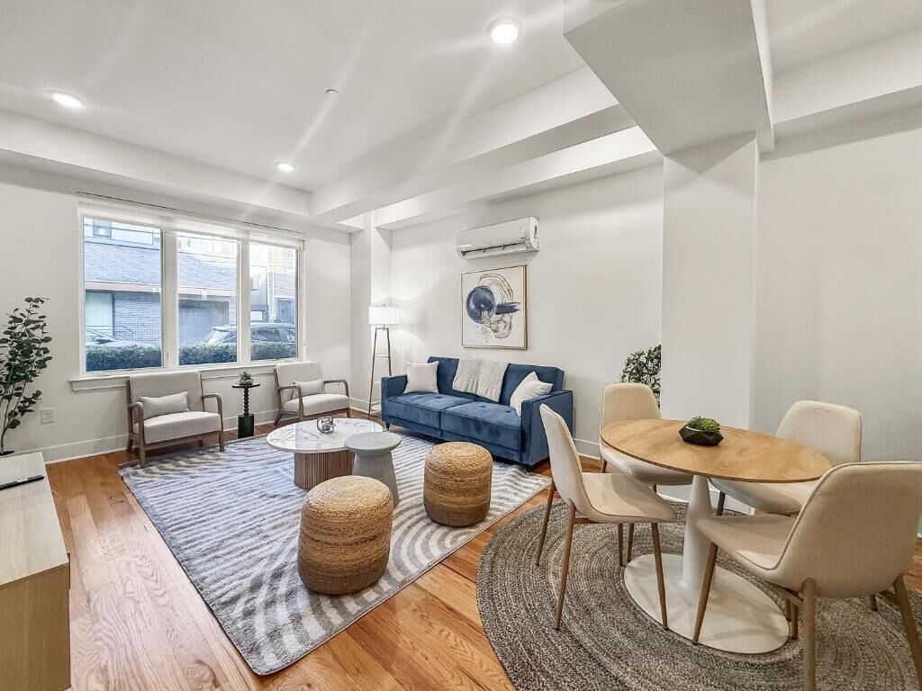 A modern living room with a blue sofa, round coffee table, and a dining area with a wooden table and chairs.