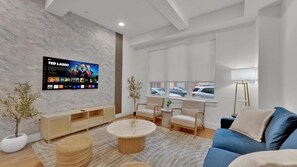 A modern living room with a flat-screen TV, a blue sofa, a round coffee table, and a wooden cabinet. - Apartmint at Liberty B Philadelphia (Philadelphia)