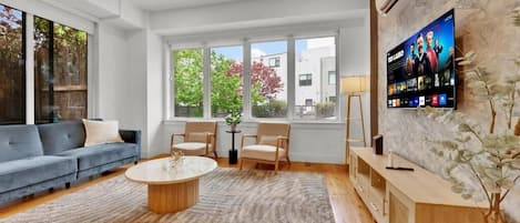 A living room with a sofa, chairs, a coffee table, a TV, and a plant.