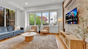 Ein Wohnzimmer mit Sofa, Sesseln, einem Couchtisch, einem Fernseher und einer Pflanze.
