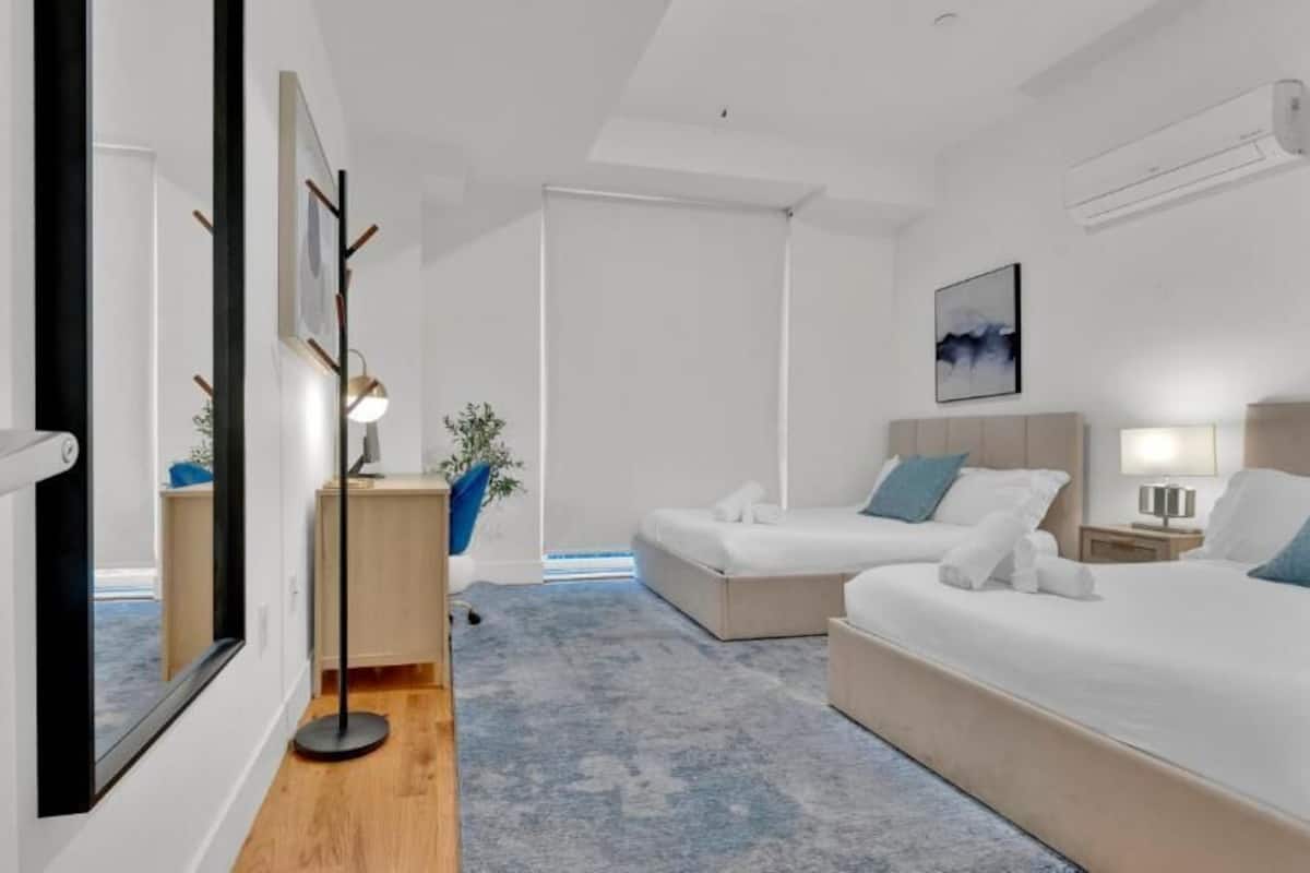 Une chambre d’hôtel moderne avec deux lits, un bureau, une chaise, une plante et des œuvres d’art accrochées aux murs.