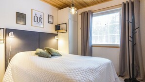Ein ordentlich bezogenes Bett mit gesteppter Decke, einer Nachttischlampe und einem Fenster mit Vorhängen.