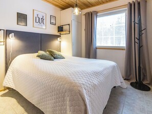 A neatly made bed with a quilted cover, a bedside lamp, and a window with curtains. - Luonnonrauha a by Interhome (Sodankylä)
