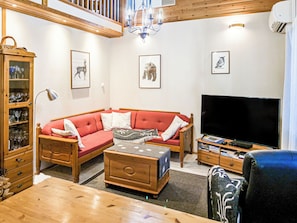 Een woonkamer met een rode bank, houten meubels, een televisie en afbeeldingen van dieren in lijsten aan de muur.
