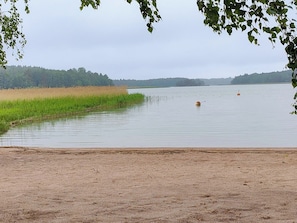 A calm lake with a sandy shore and a distant forest. - Rustholli17 by Interhome (Salo)