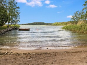 A calm river with a wooden boat docked on the left, surrounded by trees and a sandy shore.
