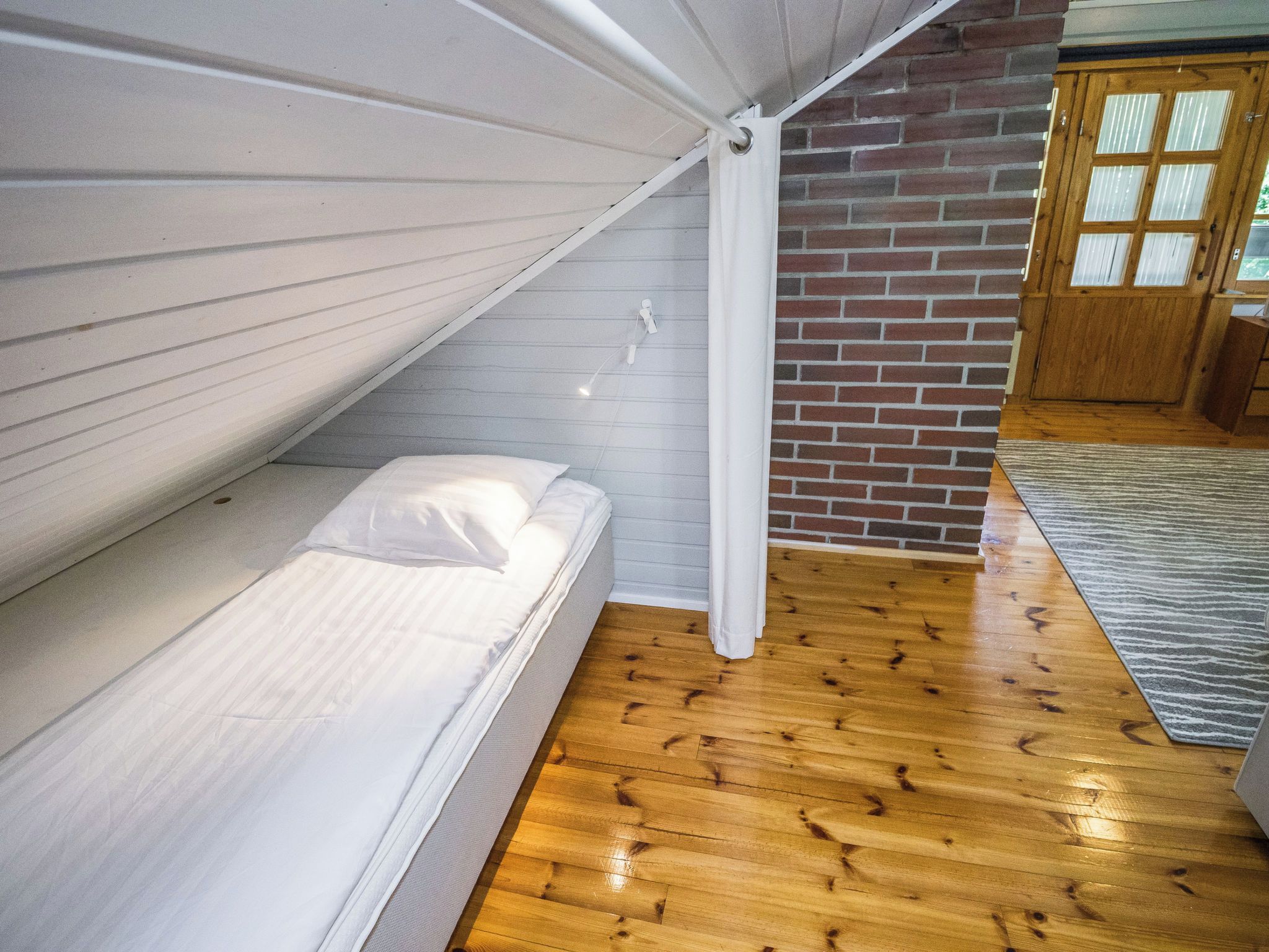 A room with a bunk bed, wooden flooring, a brick wall, and a wooden door.