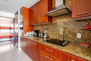 A modern kitchen with wooden cabinets, granite countertops, a stainless steel range hood, and a red decorative item. - Luxury apartment Nuevo Vallarta Villa Magna condo (Nuevo Vallarta)