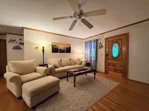 Ein Wohnzimmer mit Deckenventilator, einer Couch, einem Couchtisch, einer Lampe und einer Tür mit Buntglasfenster.